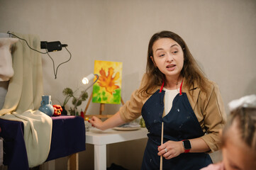 Teacher learn children to draw pictures in an art lesson. Painting in workshop. Woman drawing brush on easel. Artist explains how to mix and combine colors. Education, learning concept. Closeup.