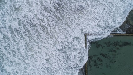 Aerial view of the contrasting turquoise pool meeting the churning white waves of the ocean's edge, Location Omitted, Location Omitted.
