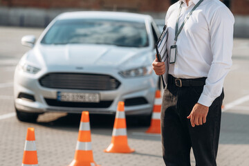 Notepad is in hands. Driving school worker is outdoors near car