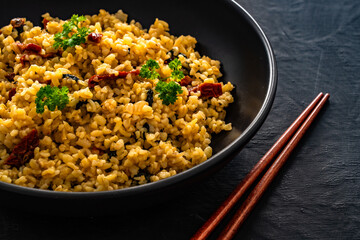Boiled bulgur with sun dried tomatoes and parsley on black background	