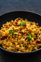 Boiled bulgur with sun dried tomatoes and parsley on black background	