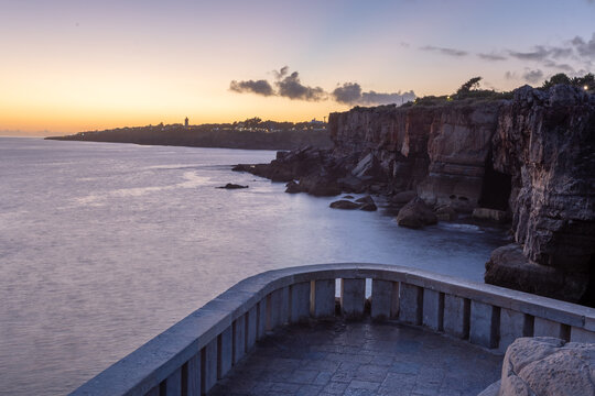 View of the dramatic cliffs of Boca do Inferno meet the Atlantic under a serene sky, the stone terrace offering a silent stage for nature's spectacle, Cascais, Lisboa, Portugal.