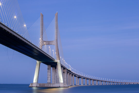 View of Ponte Vasco da Gama bridge stretches gracefully across the tranquil waters, its illuminated cables creating a mesmerizing pattern against the twilight sky, Lisboa, Portugal.