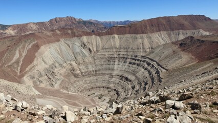 A high-angle, panoramic view of a large, circular, open-pit mine.  Colorful layers of earth and rock are visible within the excavation.