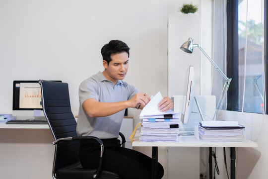 Businessman searching through piles of business documents on desk. Concept of office work, report analysis, and document organization.