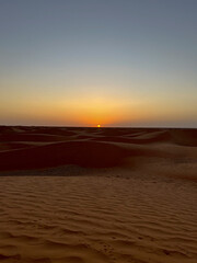 Golden sand dunes stretch endlessly across the landscape in Douz, Tunisia, reflecting the warm light of the sun. The serene desert scene captivates with its natural beauty.