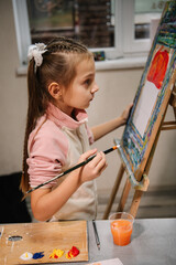 Girl enjoys painting in workshop. Art lesson. Education and learning concept. Child draw a picture in art class. School kid drawing with brush landscapes on easel. Mix and combine colors.