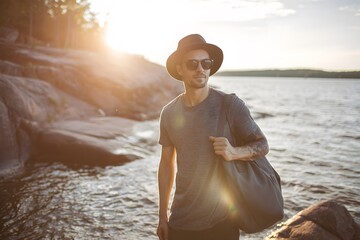 A man with a hat carries a bag by the rocky shore at sunset.