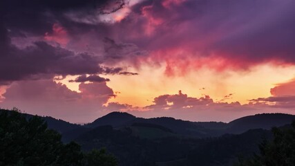 Vibrant clouds in orange, purple, and grey sweep across the sky above dark mountain silhouettes, creating a mesmerizing evening landscape. - Powered by Adobe
