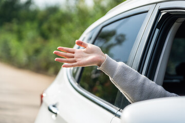 A person's hand is extended out of a car window while in an outdoor environment with greenery visible.