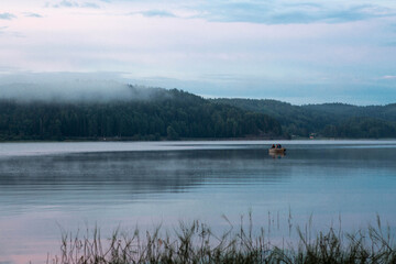 Beautiful evening foggy landscape. Lake Ladoga with a fishing boat in the fog. Beautiful natural background. Republic of Karelia, Russia.