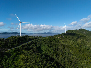 wind turbine stands by a lush, coastal area under a partly cloudy sky