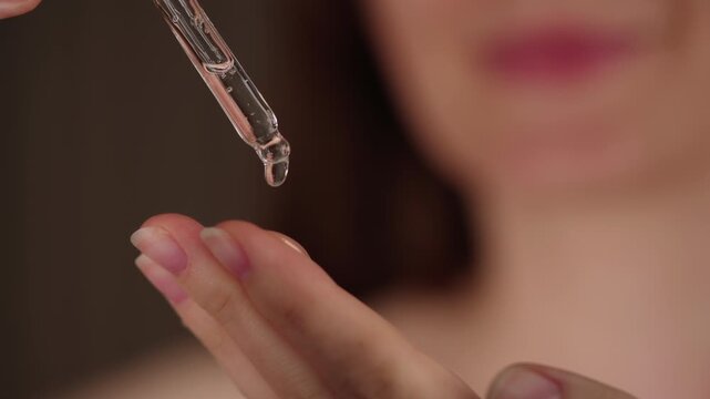 Young woman holding a dropper with serum for face. Facial oil fall from a glass pipette, macro view. Selective focus. Cosmetic background with liquid skincare product. Beauty treatment concept.
