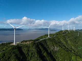 wind turbine stands by a lush, coastal area under a partly cloudy sky