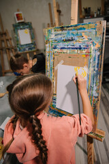 Childs draw pictures in art class. Group of school children drawing with brush landscapes on easel. Kids enjoy painting in workshop. Art lesson. Education and learning concept. Mix and combine colors.