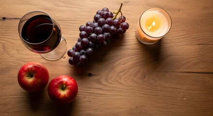 Overhead shot of a romantic arrangement featuring red wine, fresh grapes, juicy apples, and a lit candle, set on a warm wooden surface.