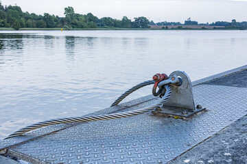 Close up of strong steel cable anchored to metal plate on riverside pier