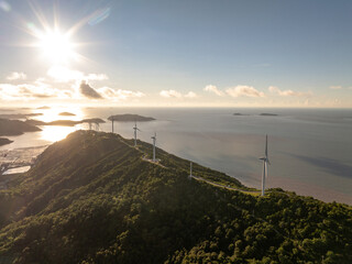 wind turbine stands by a lush, coastal area under a partly cloudy sky © zhu difeng