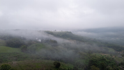 Aerial of Village in rain cloud cover tropical green mountain. Rainy season. Misty cover green forest. beautiful green village