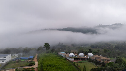 Fototapeta premium Aerial of Village in rain cloud cover tropical green mountain. Rainy season. Misty cover green forest. beautiful green village