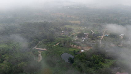 Aerial of Village in rain cloud cover tropical green mountain. Rainy season. Misty cover green...