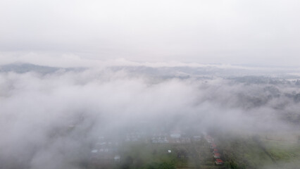Aerial of Village in rain cloud cover tropical green mountain. Rainy season. Misty cover green forest. beautiful green village