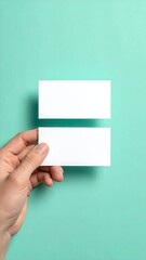 Hand holding two blank business cards against a mint green background