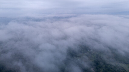 Aerial of Village in rain cloud cover tropical green mountain. Rainy season. Misty cover green forest. beautiful green village