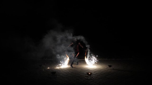 The artist of the fire show throws fire sparks into the air. It's an impressive and beautiful performance, with fire and fireworks, in slow motion. A professional circus performer dances with fire. 