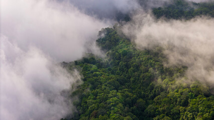 Aerial of Village in rain cloud cover tropical green mountain. Rainy season. Misty cover green...