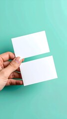 A hand holds two blank white business cards against a teal background