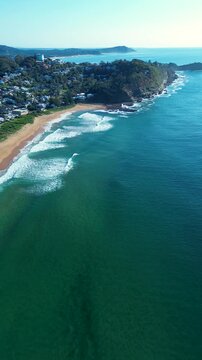 Drone aerial portrait of ocean waves crashing on sandbar at beautiful North Avoca Beach with residential housing and water tank tower on bushland coastline headland Central Coast Australia travel