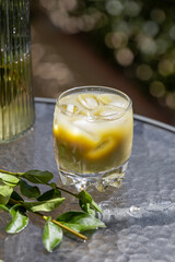 Vibrant iced matcha latte with ice and a green sprig, on an outdoor table under natural light. A refreshing, healthy beverage perfect for a cool sunny day.