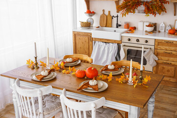 Dining table is elegant set for autumn holidays Halloween or Thanksgiving day, with orange pumpkins, plates with napkins and colorful leaves, creating a warm and inviting atmosphere in rustic kitchen