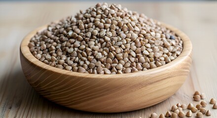 Fototapeta premium A wooden bowl is piled high with a mound of raw, uncooked buckwheat groats on a light wooden surface