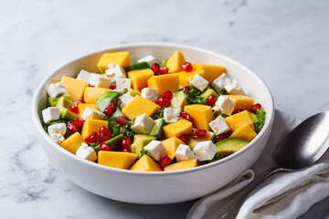 Avocado, mango, pomegranate, and feta cheese salad in a white bowl.