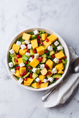 Avocado, mango, pomegranate, and feta cheese salad in a white bowl.