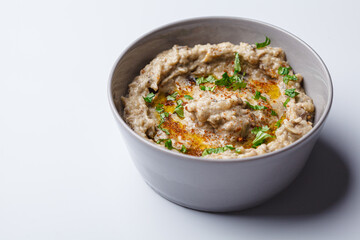 Baba ganoush - spread of baked eggplant with tahini and spices in gray bowl on white background.