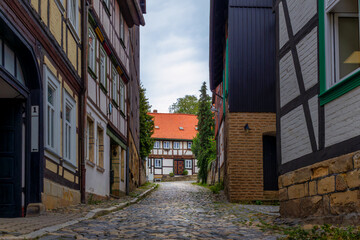 Narrow Cobblestone Street Winds Between Traditional Half-timbered Houses Leading Toward A Red-roofed Building In The Distance