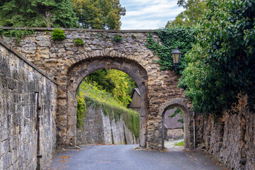 Two Ancient Stone Arches Covered In Ivy And Weathered Brick Create A Narrow Inviting Alleyway...