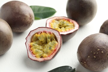 Fresh passion fruits with green leaves on white table, closeup