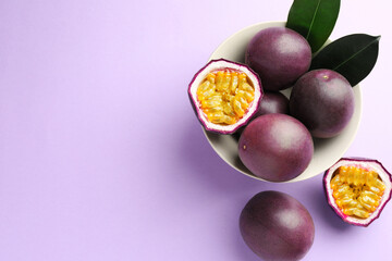 Fresh passion fruits with green leaves on violet background, flat lay. Space for text