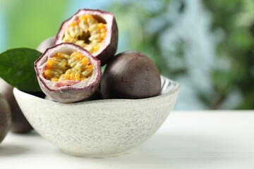 Fresh passion fruits in bowl on white wooden table outdoors, closeup. Space for text