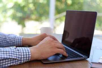 Fototapeta premium Man working on laptop at wooden table indoors, closeup