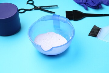 Care cosmetic product for blonde hair in bowl and hairdresser's tools on light blue background, closeup
