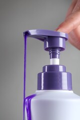 Woman with bottle of hair care product for blonde hair on grey background, closeup