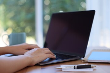 Fototapeta premium Woman working with laptop at table against blurred background, closeup