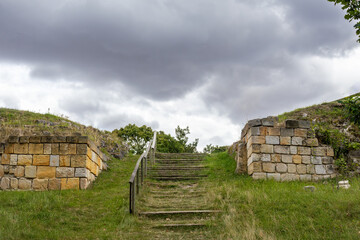 Flight Of Stone Stairs With A Rustic Railing Climbs A Grassy Hill Between Two Ancient Stone...