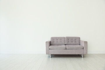 Comfortable gray sofa near white wall in room, space for text