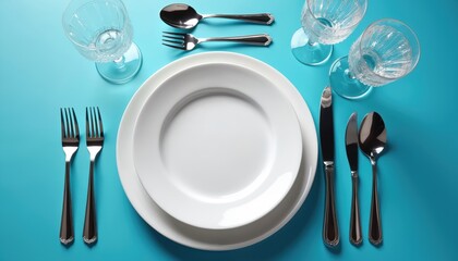 Overhead view of elegant table setting with white plates and silver cutlery on trendy blue background. Formal dinner place setting for dining with glassware. Clean design for minimalist style event.